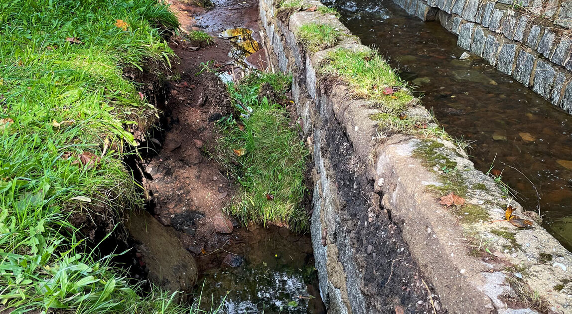 Przykład wpływu pierwotnych uszkodzeń muru oporowego w postaci ubytków i spękań na uszkodzenia popowodziowe stabilizującej zasypki gruntowej za konstrukcją muru