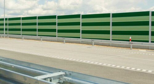 Ekran akustyczny ustawiony wzdłuż autostrady z jezdnią i barierą ochronną.