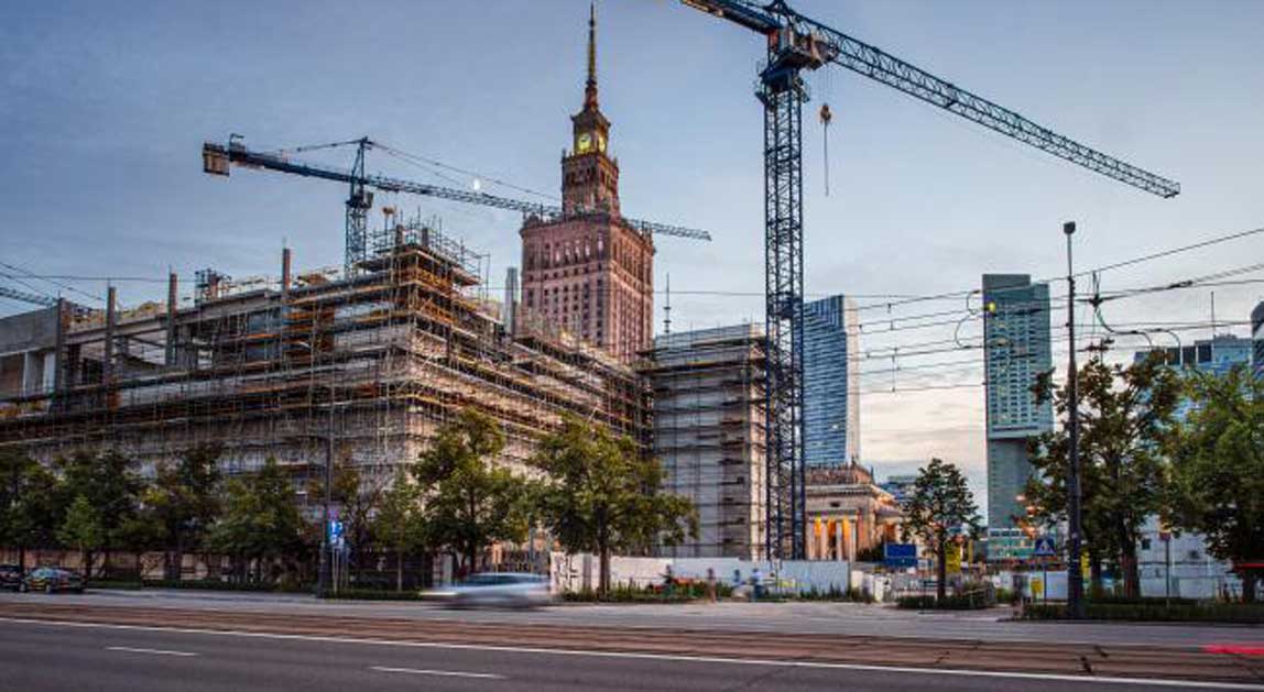 Budowa prowadzona na terenie poprzemysłowym w Warszawie z widocznymi żurawiami budowlanymi i zabudową miejską.