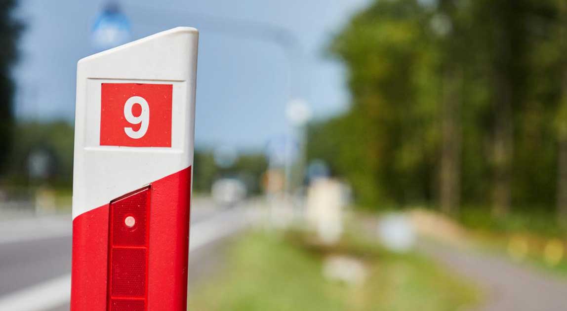 Biało-czerwony słupek drogowy z numerem 9 stojący przy jezdni.
