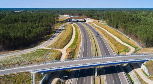 Droga ekspresowa przebiegająca przez teren leśny z wiaduktami i drogami serwisowymi.