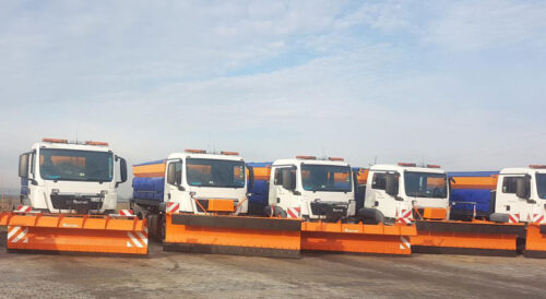 Samochody ciężarowe wyposażone w pomarańczowe pługi przygotowane do zimowego utrzymania dróg