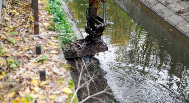 Koparka oczyszczająca umocnione koryto miejskiej rzeki w Katowicach