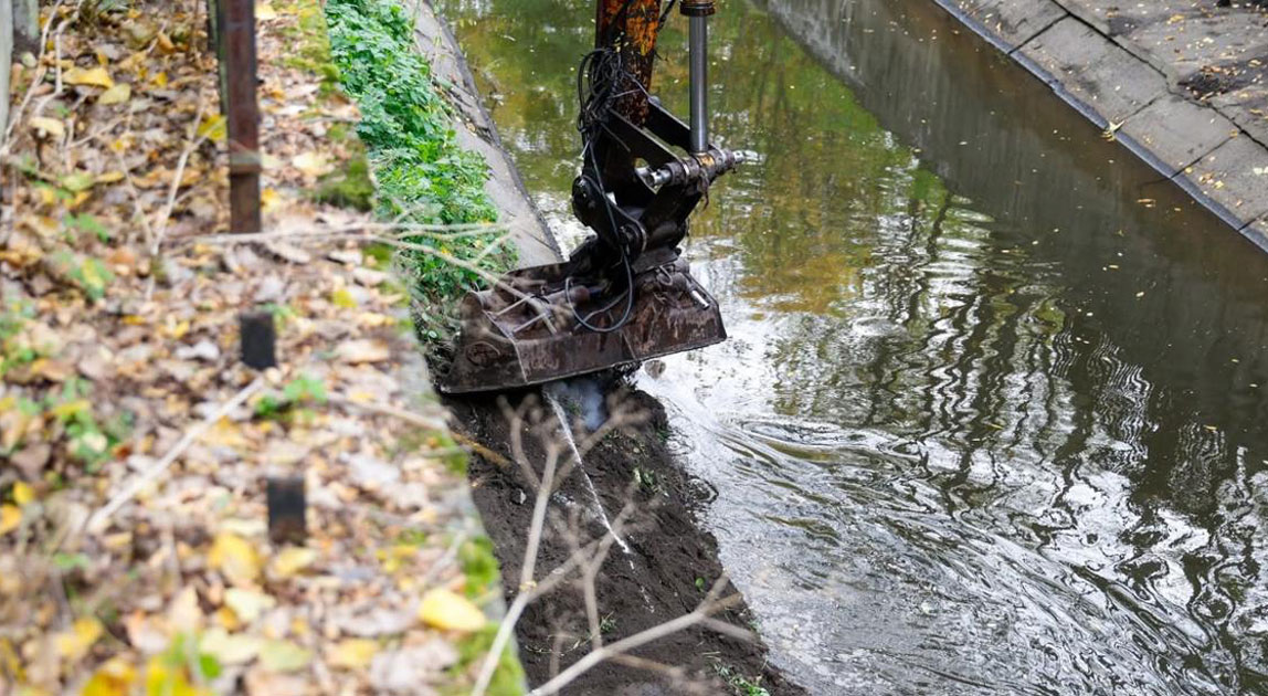 Koparka oczyszczająca umocnione koryto miejskiej rzeki w Katowicach